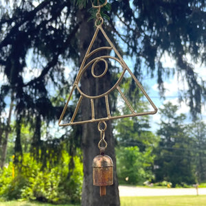 A wind chime featuring a gold all seeing eye hanging from a pine tree.