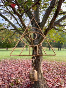 A wind chime featuring a gold all seeing eye hanging from a tree in a park