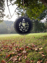 Decorative wind chime with Ganesha design hanging in a park with grass and trees.