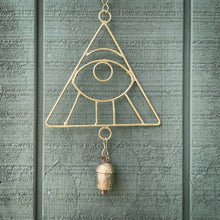 A wind chime featuring a gold all seeing eye hanging against a sage green shed.