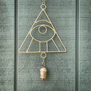 A wind chime featuring a gold all seeing eye hanging against a sage green shed.