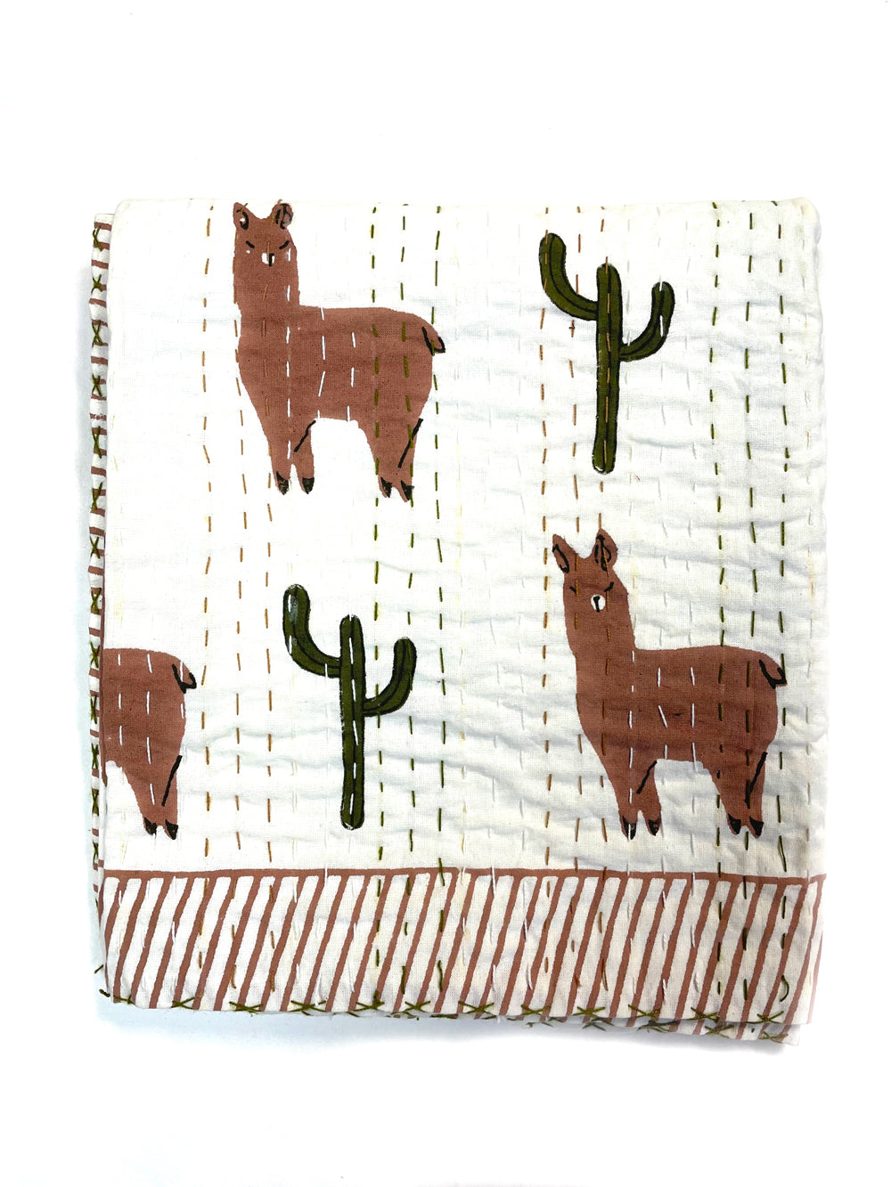 A quilt featuring llamas and cacti. Sustainable creative accessories.